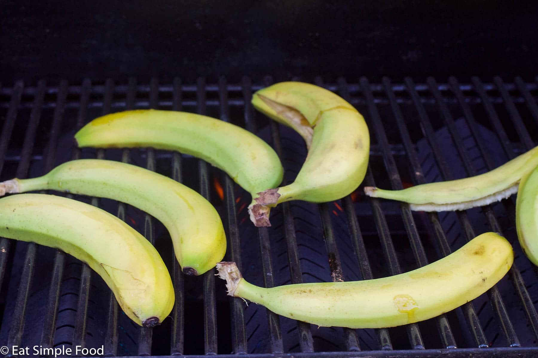 4 halved raw bananas with the peel on and one whole bananas on the grill starting to cook.