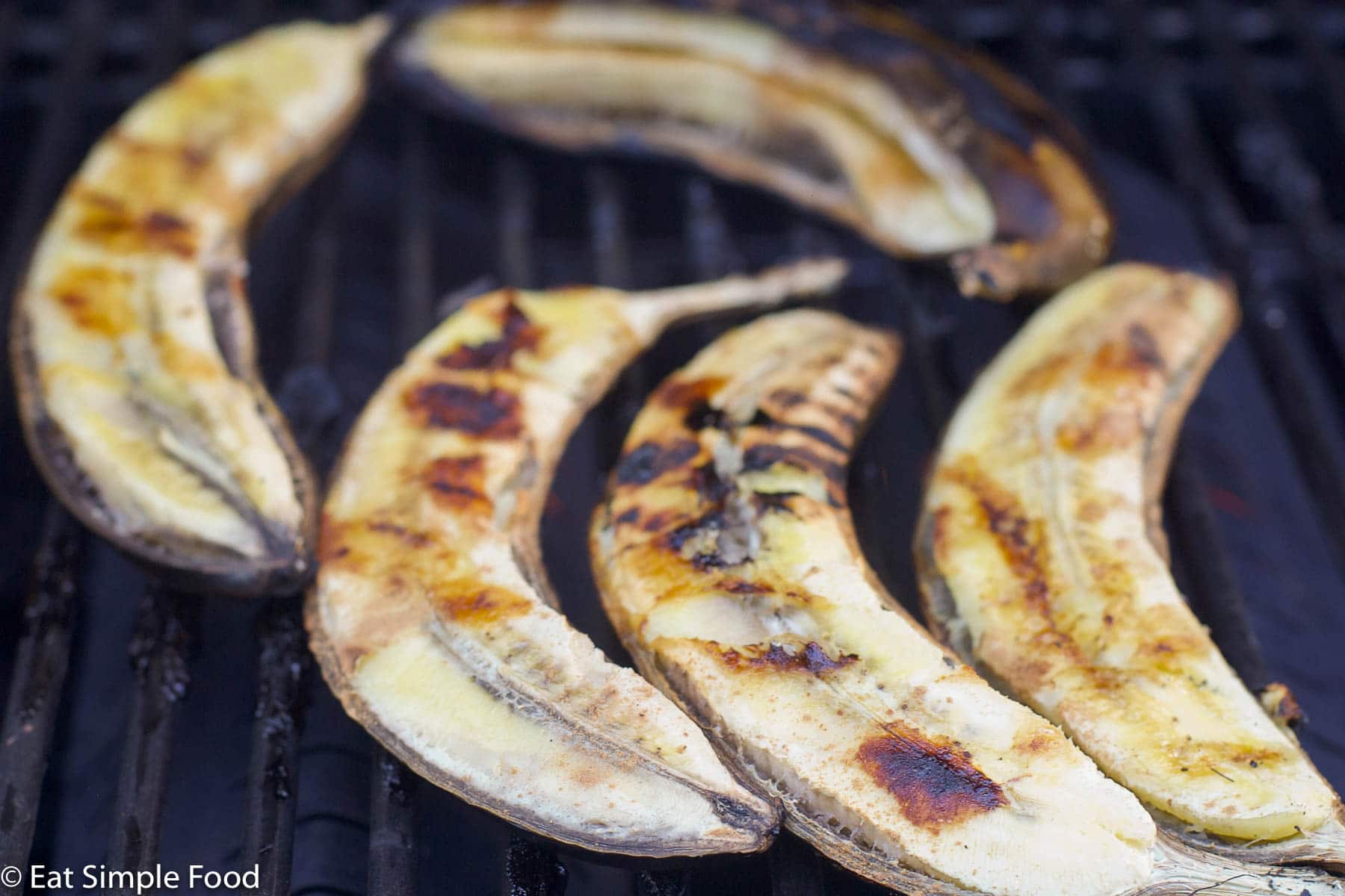 5 halved bananas with the peel on and facing down toward the grill. Flesh side facing up and browned by grill marks.