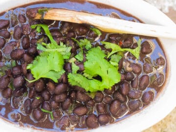 Top view of white oval bowl of black beans with a cilantro leaf garnish.