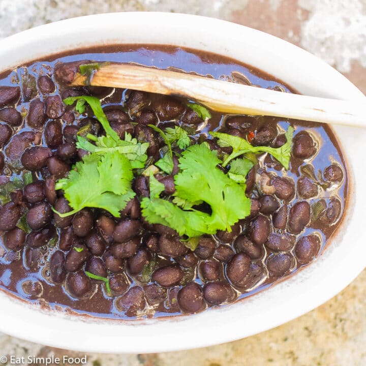 Top view of white oval bowl of black beans with a cilantro leaf garnish.