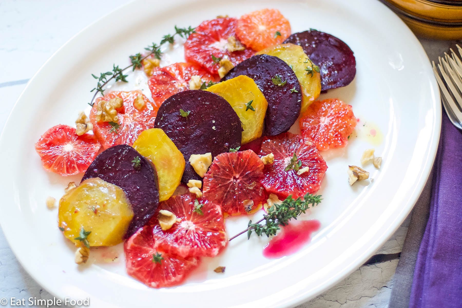 Blood Oranges & Roasted Yellow and Red Beets on a white plate with thyme and walnuts sprinkled over the top. Top view.