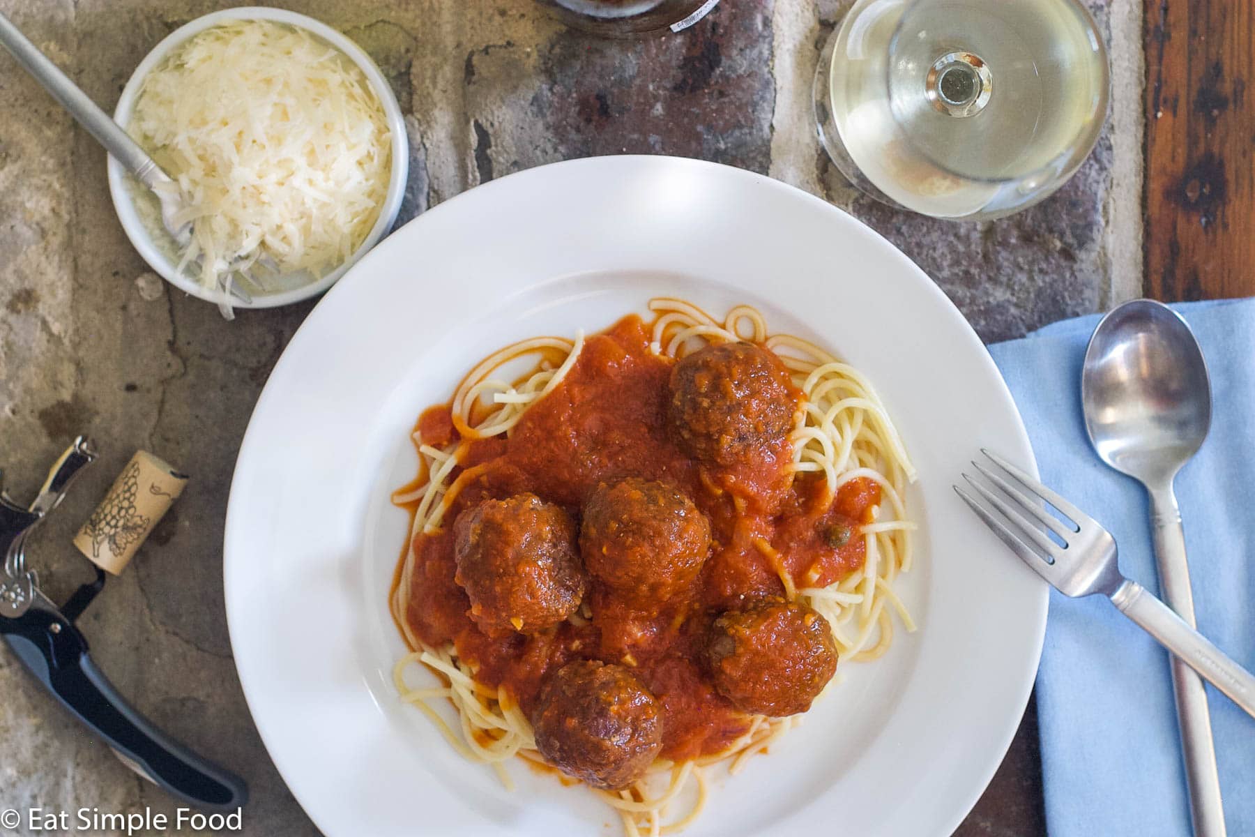 White plate of meatballs with red sauce and spaghetti with a fork and spoon. Top view.