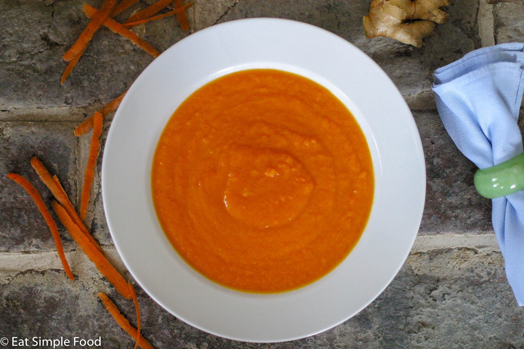 Creamy Orange Carrot Soup in A White Bowl with a brick background with carrots peels around it. Top view.