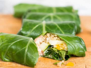 Side view of 5 collard green wraps with one cut open to expose the quinoa and vegetables inside.