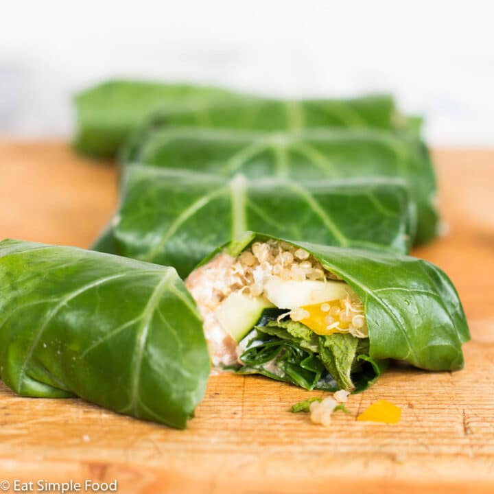 Side view of 5 collard green wraps with one cut open to expose the quinoa and vegetables inside.