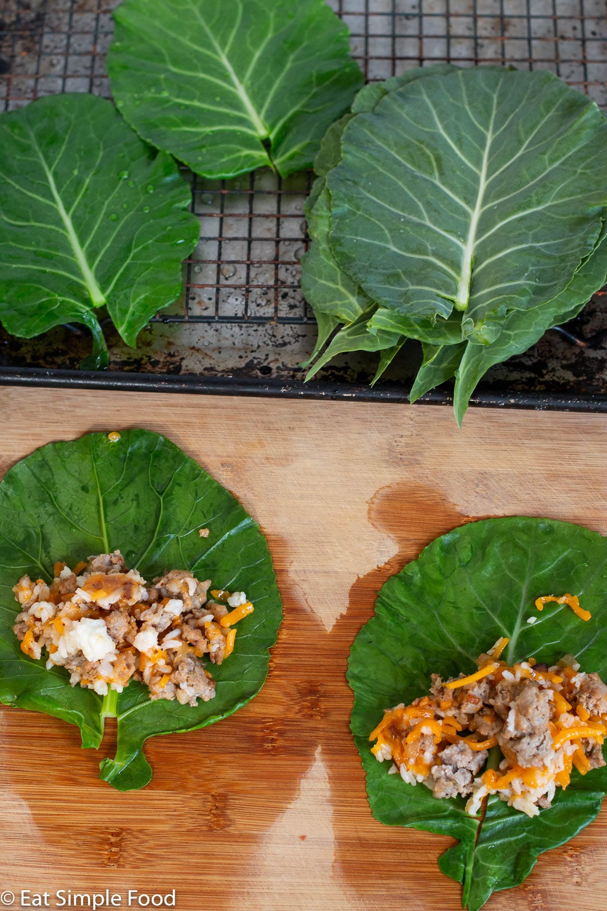 2 Sausage, cheese, and rice laying on 2 blanched collard greens getting ready to be wrapped. Collard greens laying in background on elevated wire rack.