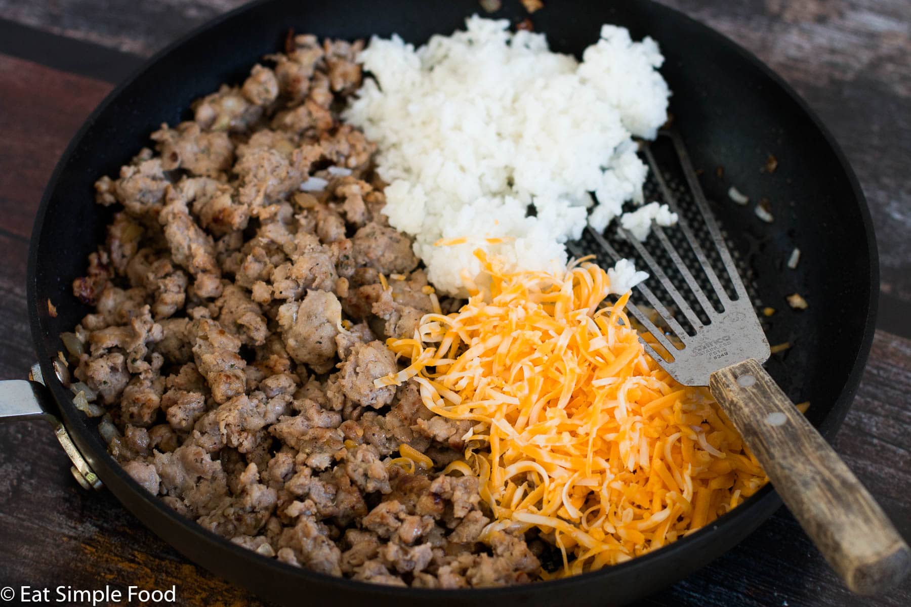 Cooked Sausage, yellow cheese, and white rice in a pan with a spatula.