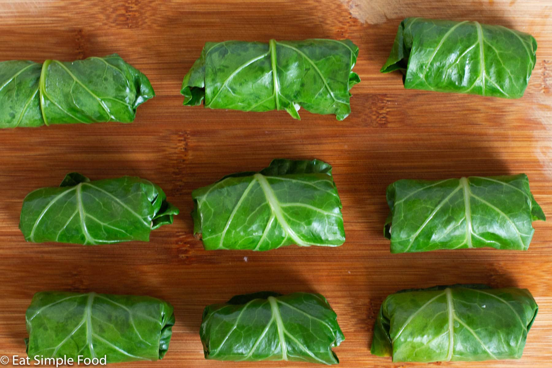 9 Sausage, cheese, and rice wrapped collard greens on a wood cutting board.