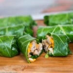 Sausage, cheese, and rice wrapped collard greens on a wood cutting board. One cut open.