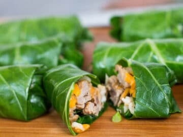 Sausage, cheese, and rice wrapped collard greens on a wood cutting board. One cut open.