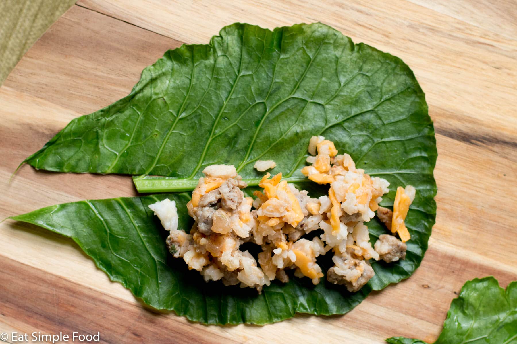 Sausage, cheese, and rice laying on a blanched collard green getting ready to be wrapped.