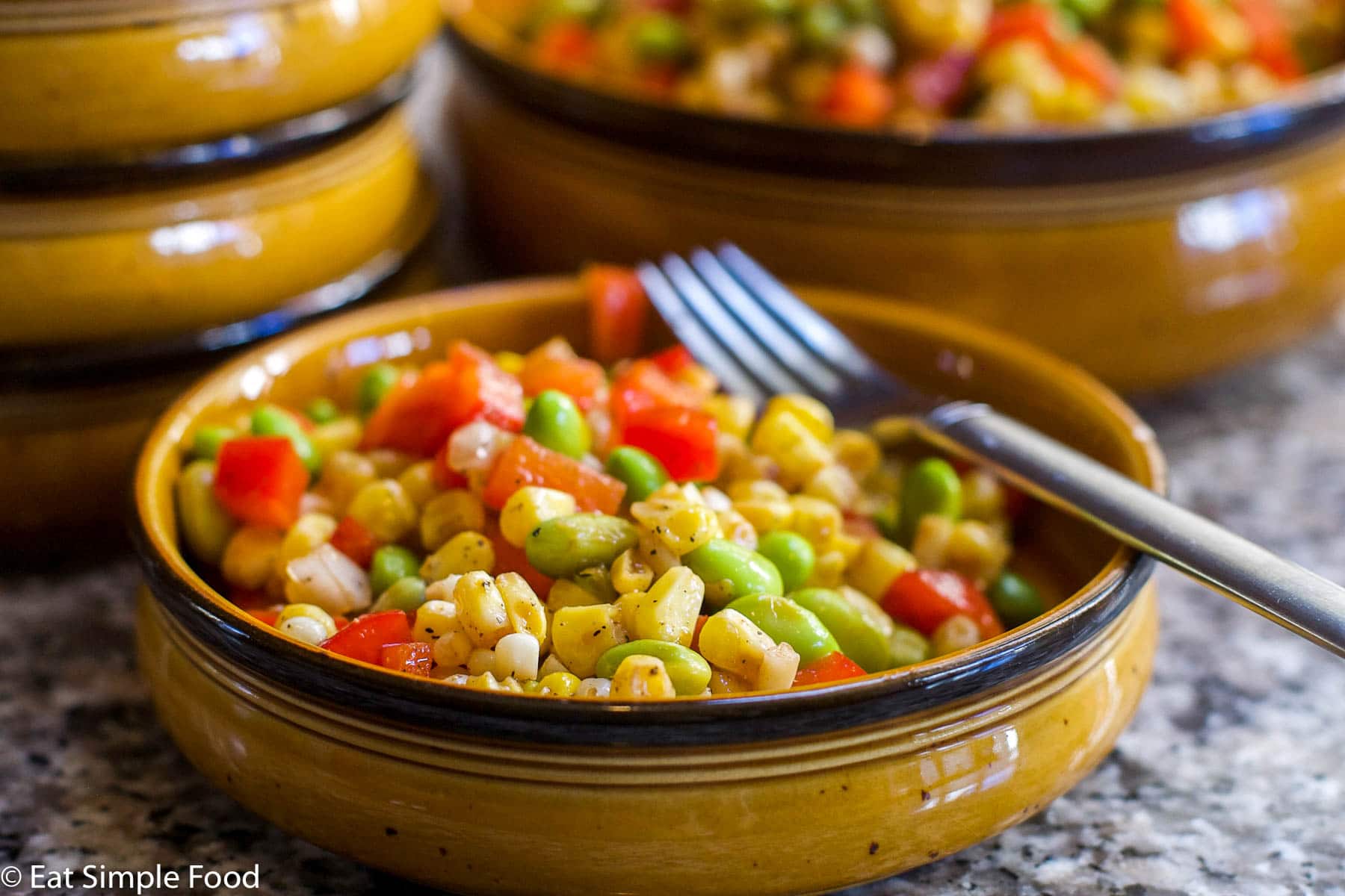 Corn, Edamame, & Red pepper Succotash with red peppers with a fork in a brown bowl. side view.