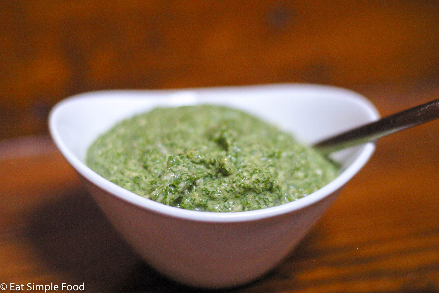 White bowl of green dill pesto with a spoon sticking out. Side view.