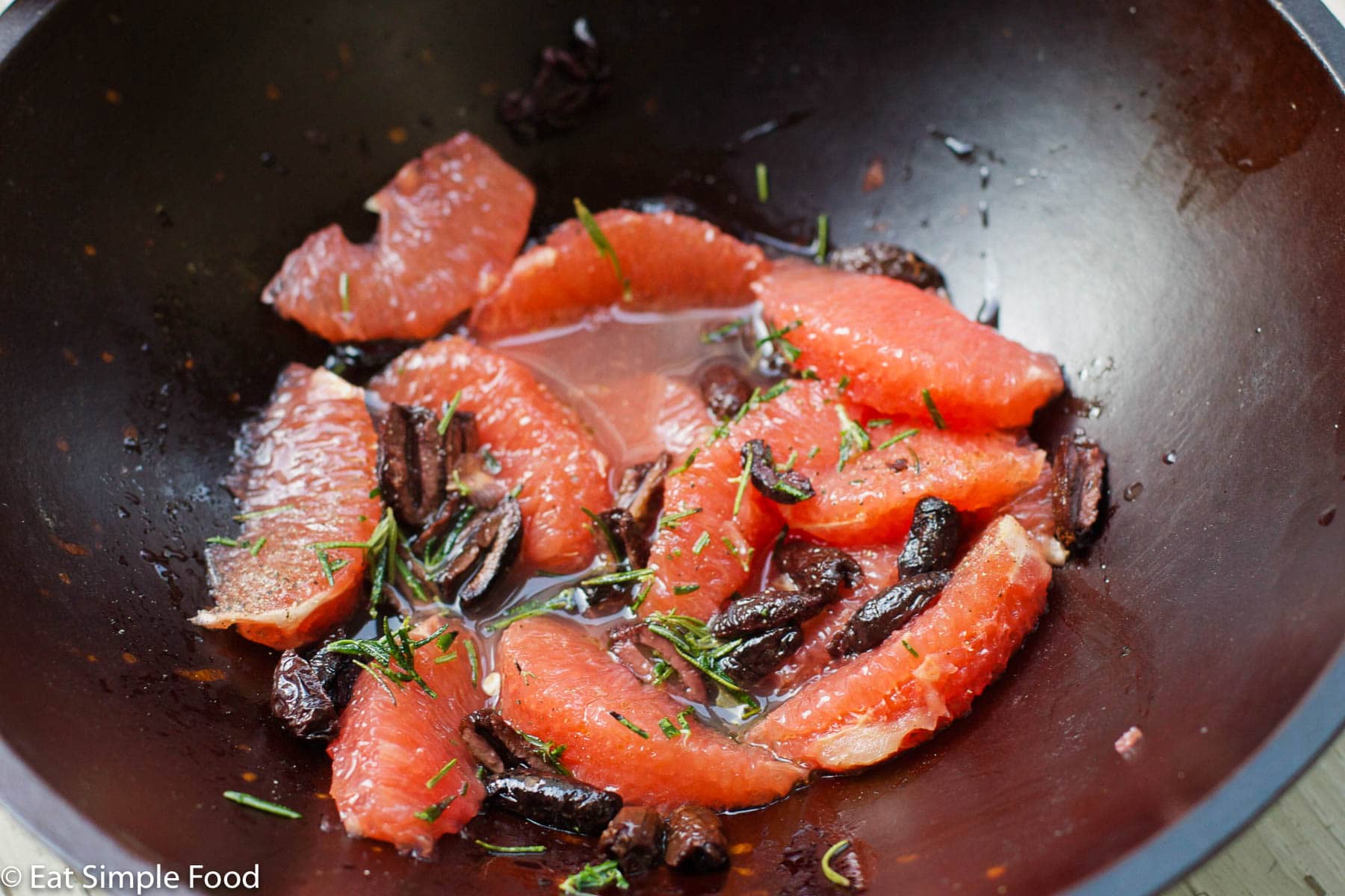 PInk grapefruit segments with black kalamata olives and fresh chopped rosemary in a wood bowl. close up. side view.