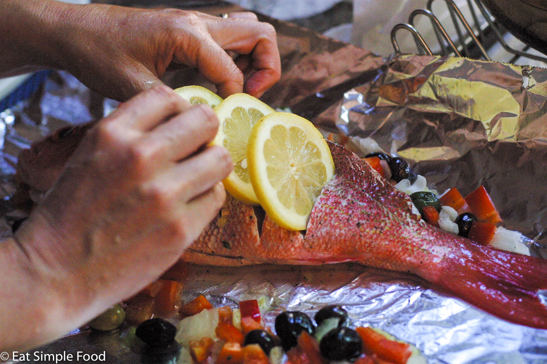 Red Snapper with slices in the whole fish and hands putting lemon slices into the fish.