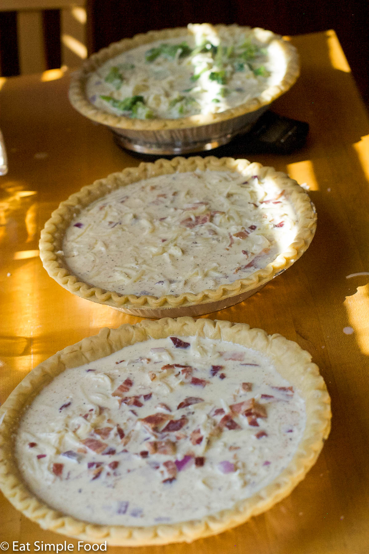 3 quiches on a wood table filled but not cooked yet. One quiche is on a scale.