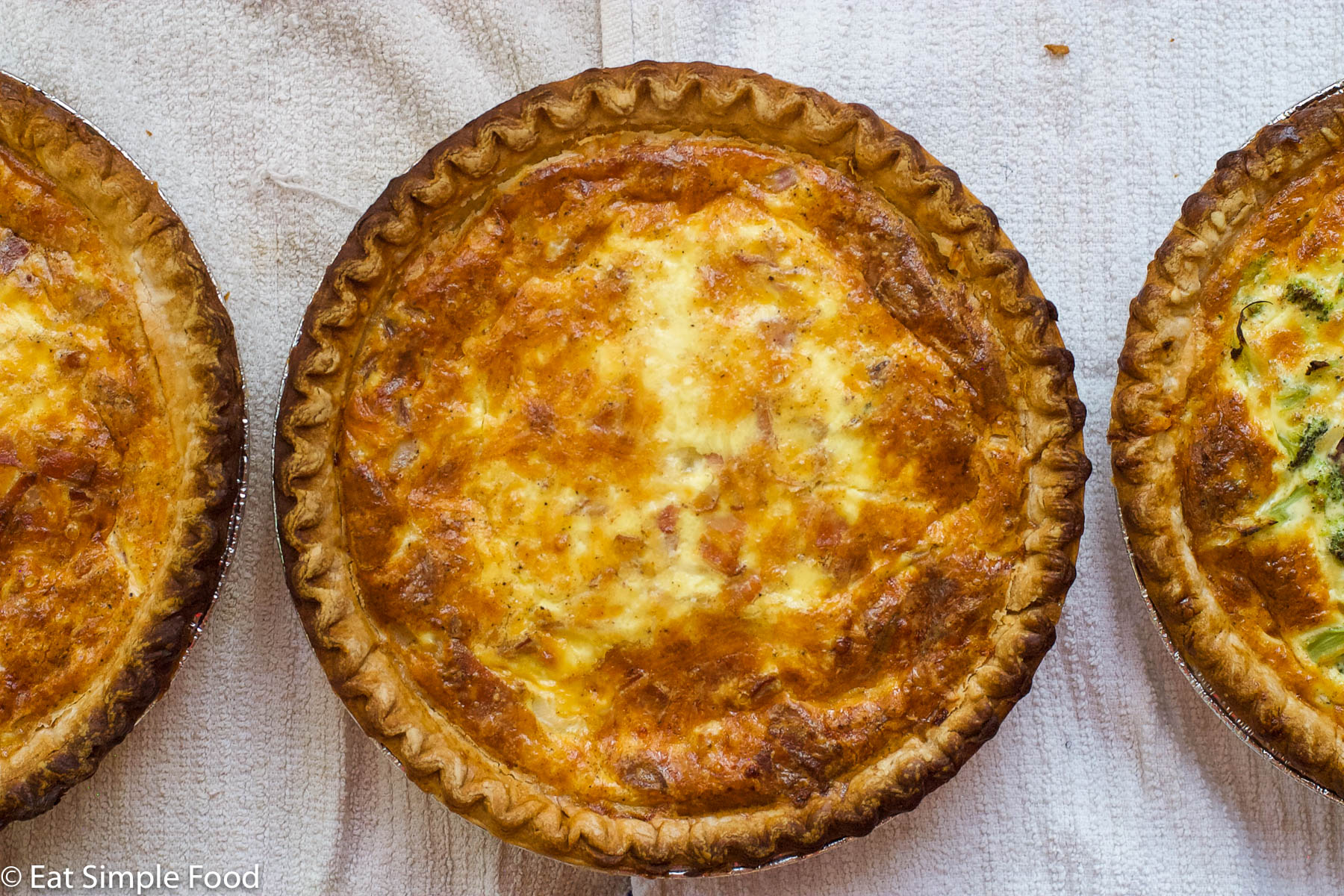 Quiche Lorraine with a partial quiche on each side. Cooked golden brown. laying on a white towel. Top view.