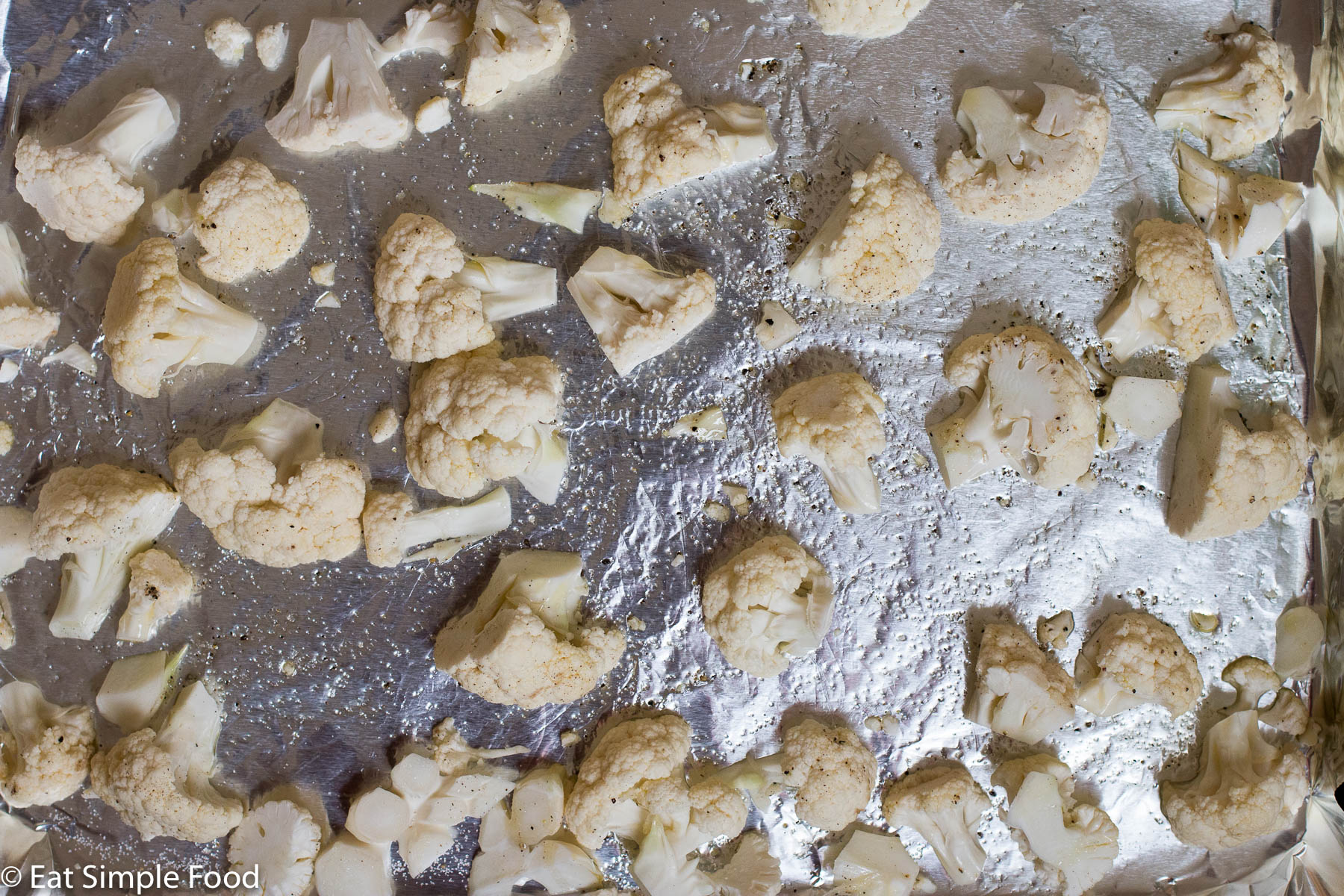 Cauliflower florets uncooked on an aluminum lined baking sheet. top view.