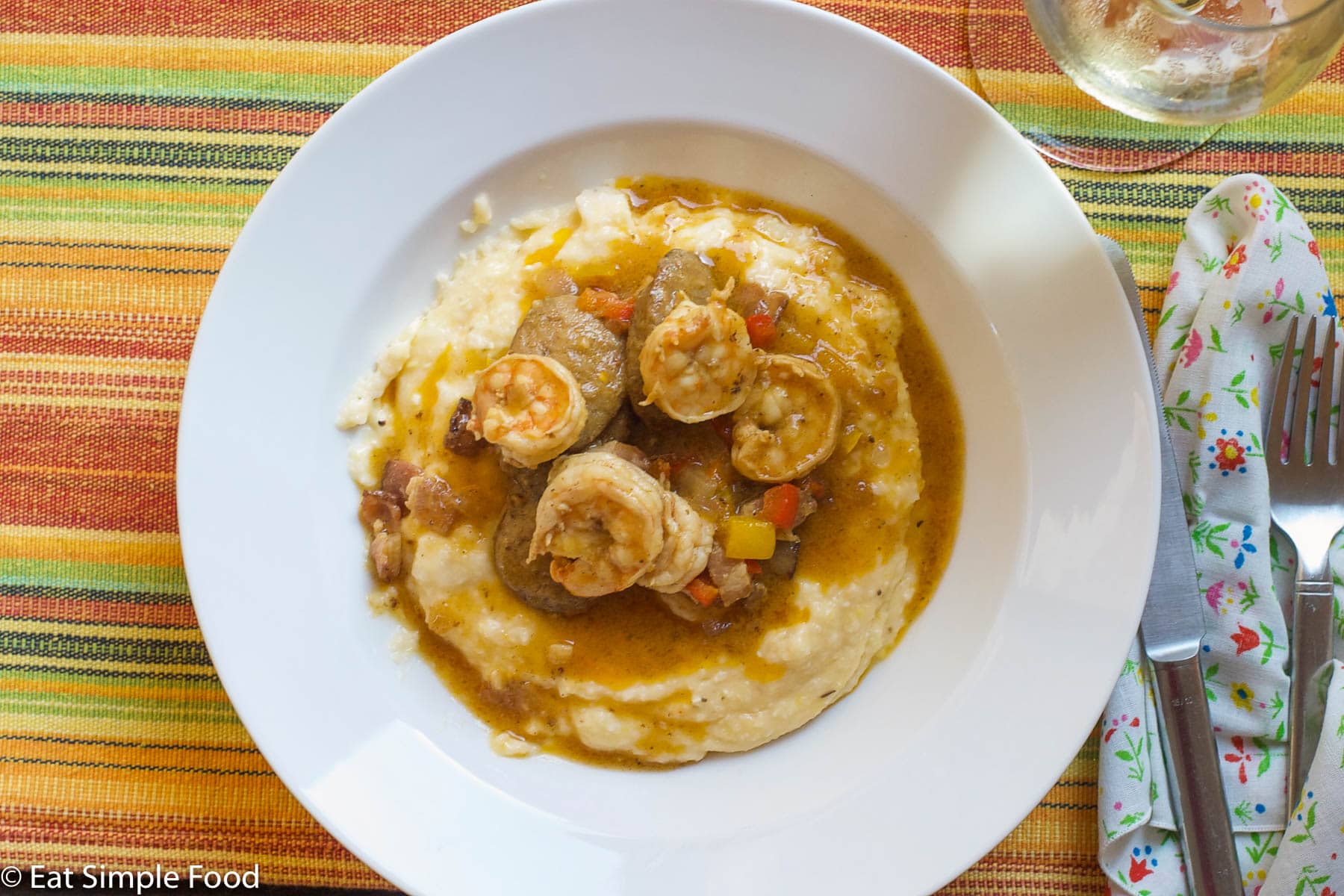 Shrimp In A Dark Roux With red and yellow peppers on yellow grits on a white plate. Top view.
