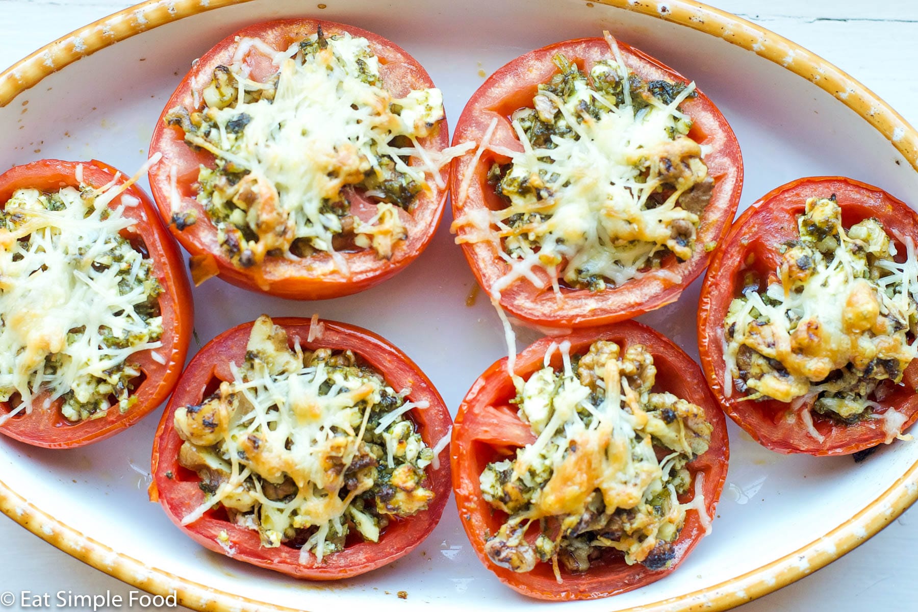 6 tomato halves filled with wild rice, basil pesto, pine nuts, and feta cheese with Parmesan cheese broiled on the top. Top view.