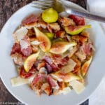Top view of a white plate with fork with quartered figs, sliced salami, shaved parmesan and croutons.