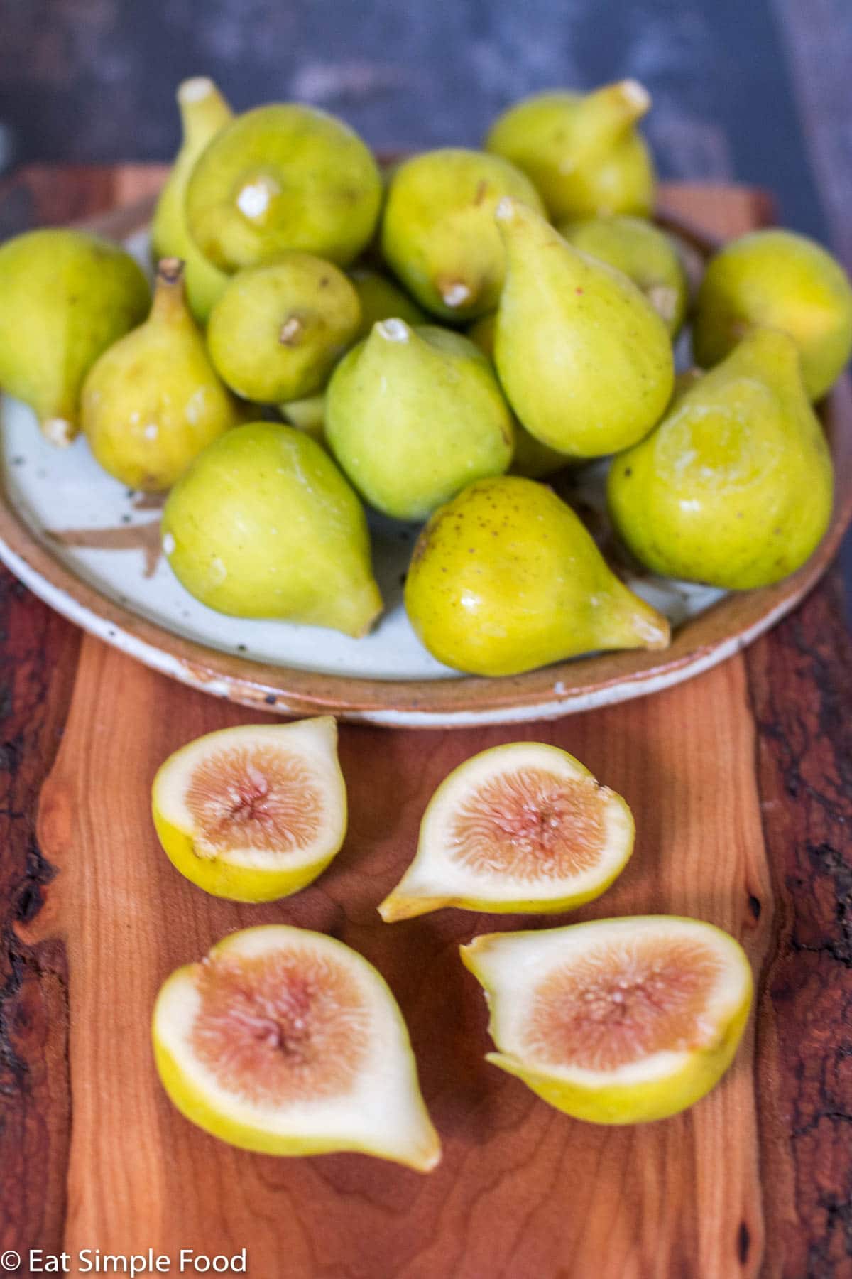 Plate of Yellow Green Figs on a cutting board with 2 figs cut in half. Side view.