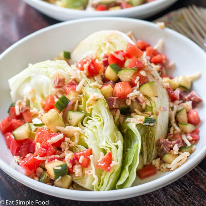 1 plates of iceberg wedge lettuce (2 wedges on each plate) topped with diced tomatoes, cucumbers, red onions, and salami in a vinaigrette.