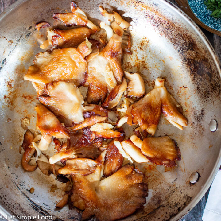 Browned mushroom caps cooked in a stainless steel pan. Top view. With a small turquoise bowl of sliced chives on the side.