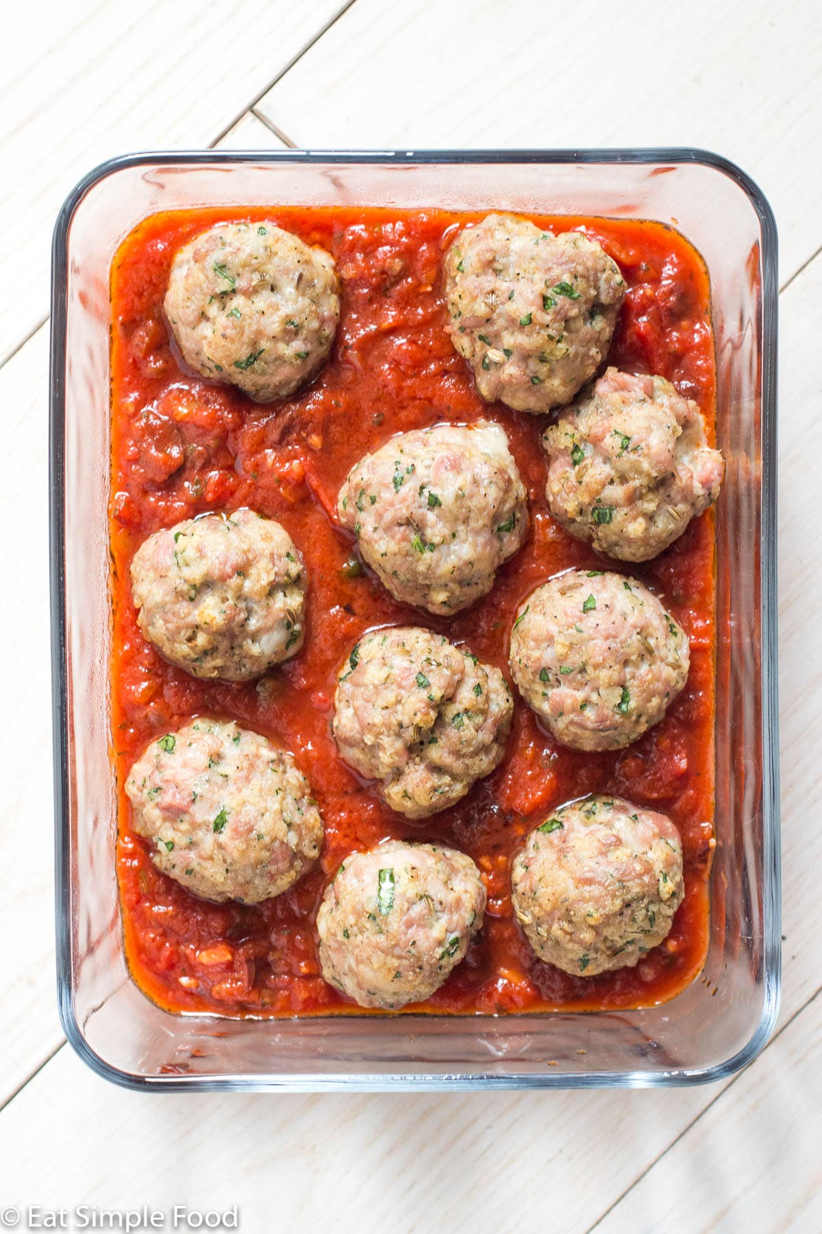 Glass pyrex rectangle dish with a red tomato sauce with 10 meatballs sitting on the sauce.