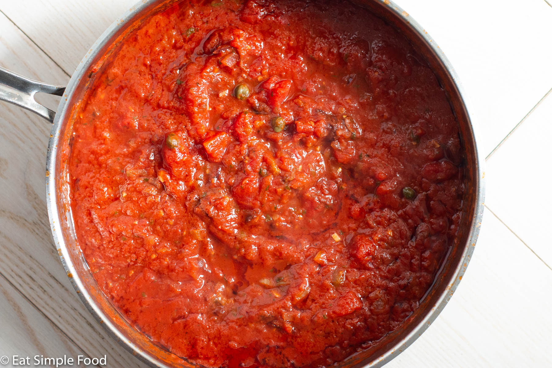 Deep stainless steel pan with a red tomato sauce with onions, garlic, and capers.