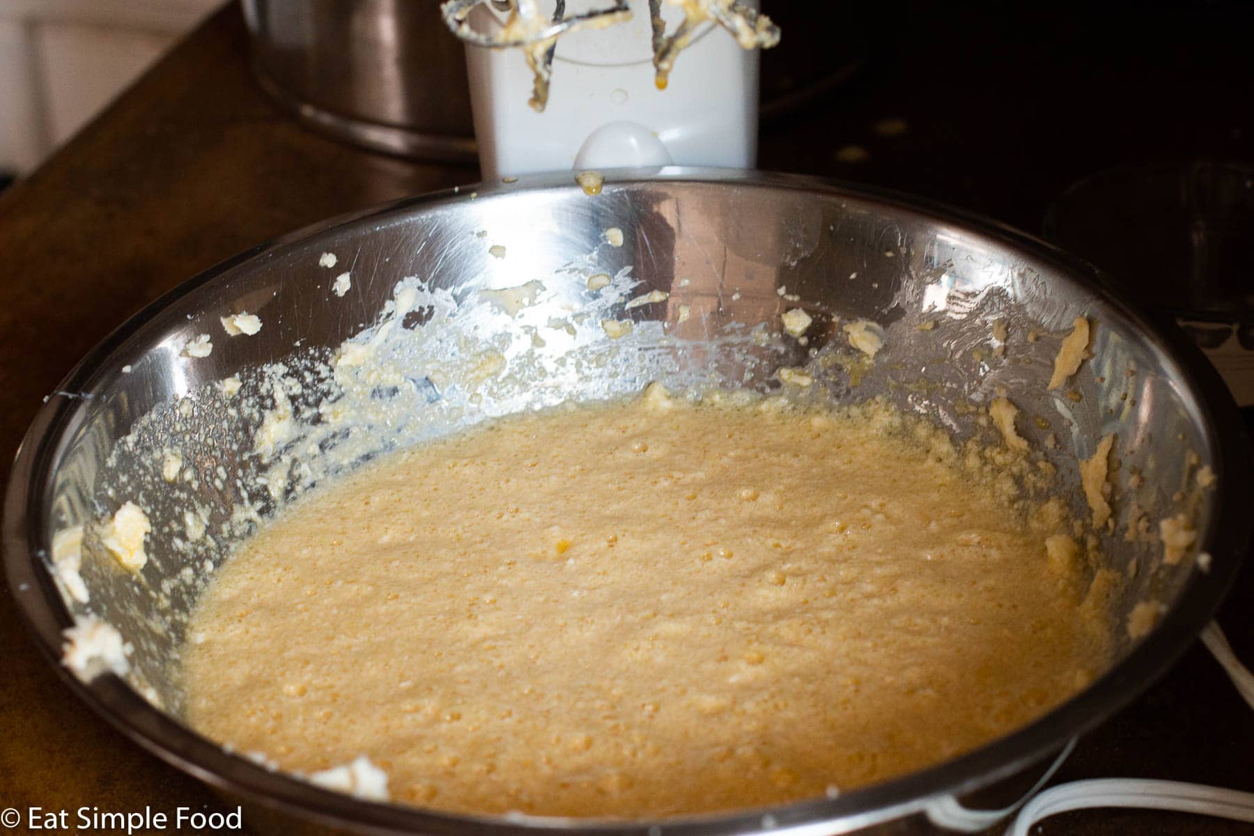 Cake batter in stainless steel bowl with hand mixer dripping above bowl.
