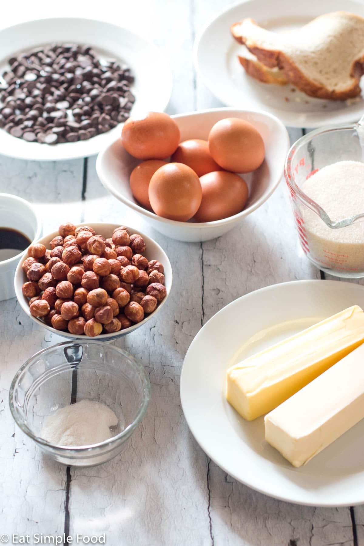 Ingredients for cake: bowl and plates of chocolate chips, whole hazelnuts, 2 sticks of butter, measuring cup of sugar, bowl of six eggs, tiny bowl of rum and baking powder.