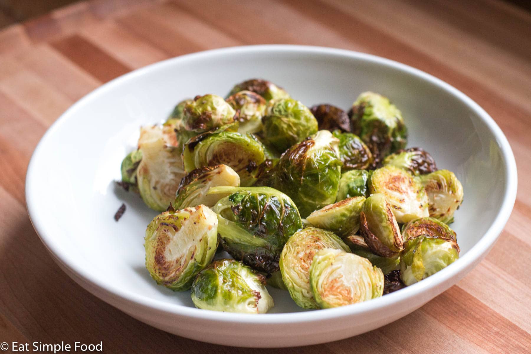 Side view of white plate of halved brown roasted Brussels Sprouts.