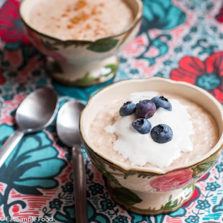 Side view of a small bowl of rice pudding with cinnamon sprinkles, whipped cream, and 5 blueberries.