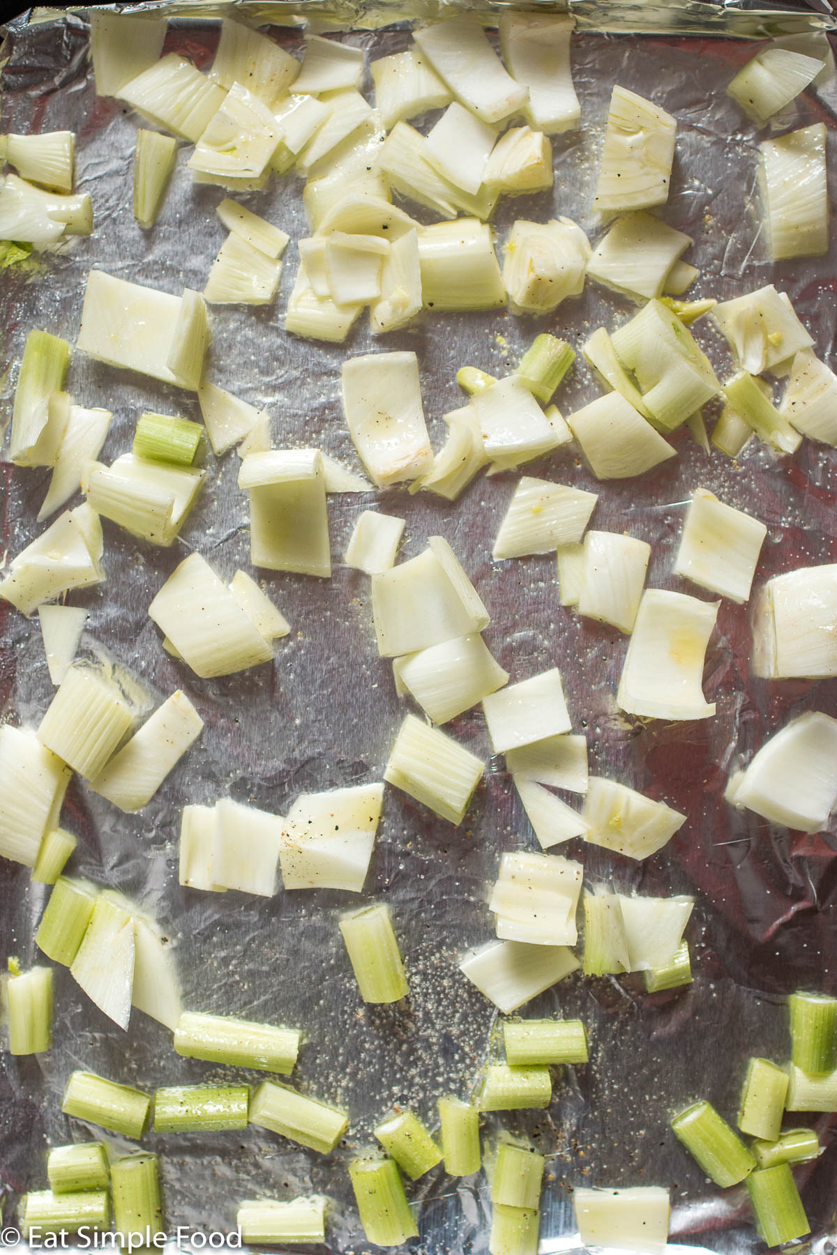 Aluminum lined sheet pan of chopped fennel spaced out evenly over the pan and dressed with olive oil, salt, and pepper. Top view.