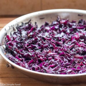 Red purple sliced cooked cabbage in a stainless steel pan on a wood table. Close up.