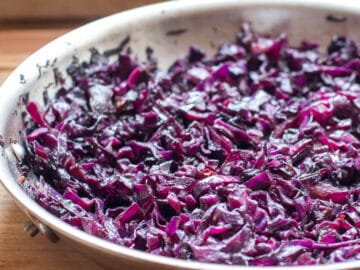 Red purple sliced cooked cabbage in a stainless steel pan on a wood table. Close up.