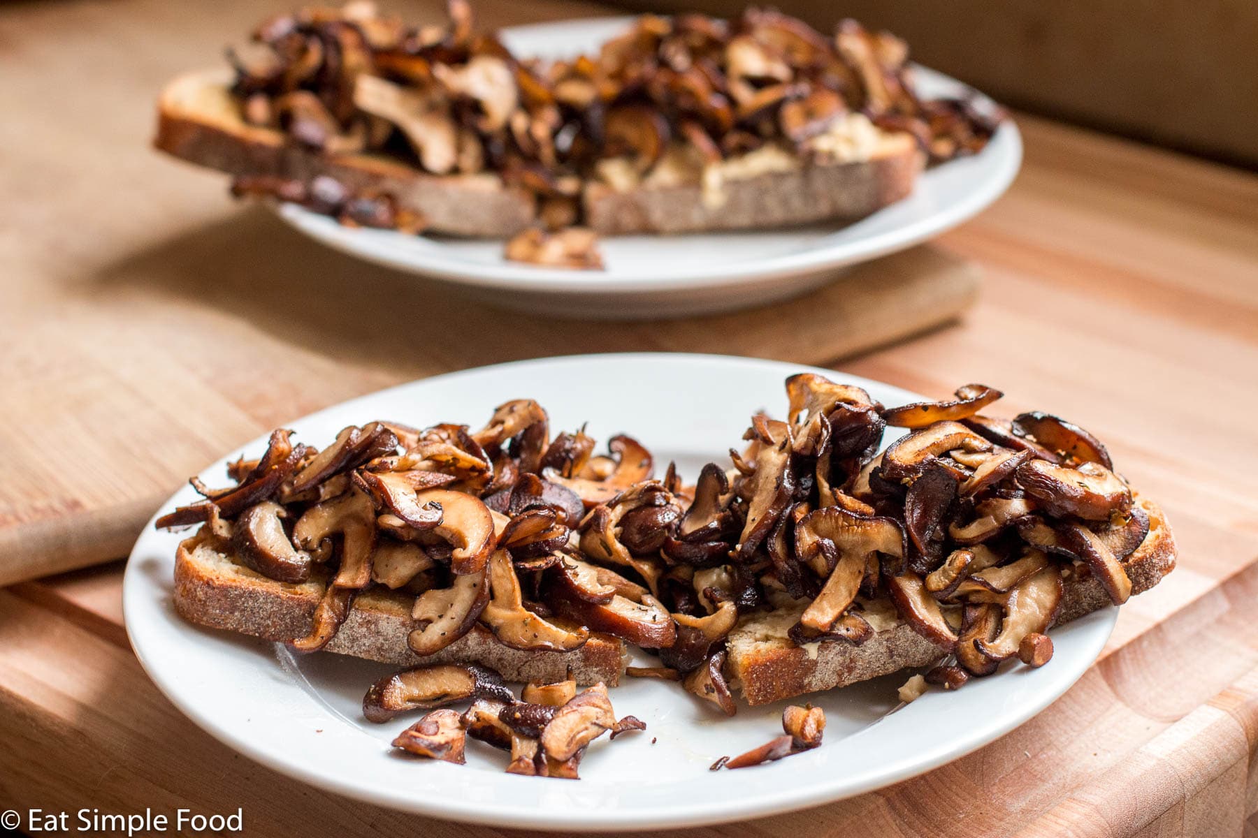 2 plates with a large piece of toast cut in half on both plates piled high with browned shiitake mushrooms.