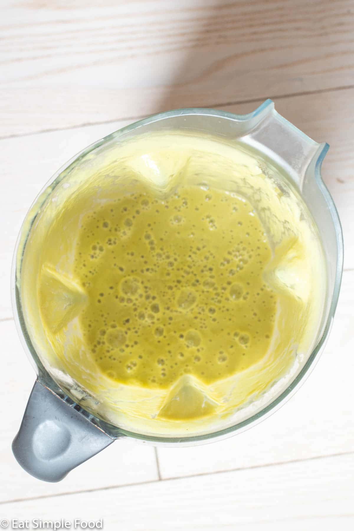 Top down view of blender filled with creamy yellow green soup.