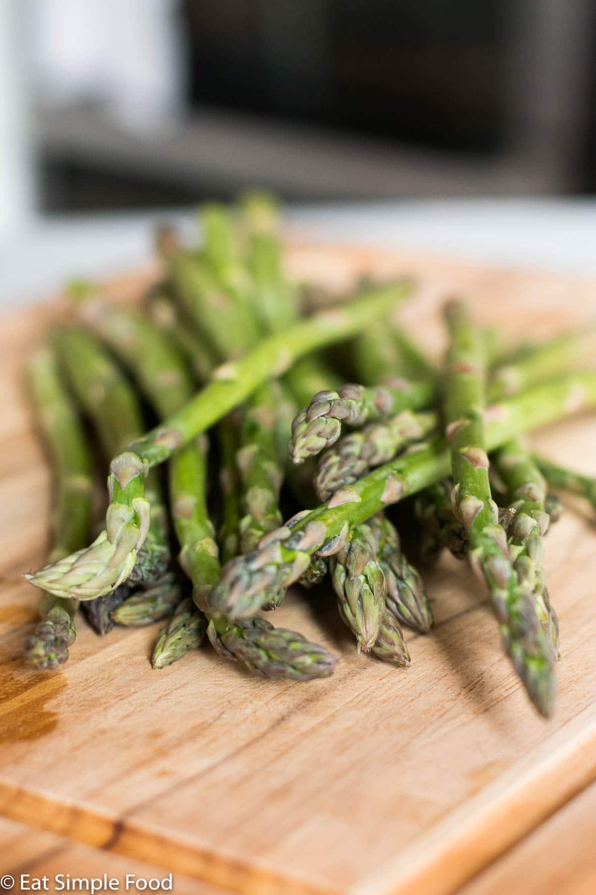 A bunch of Asparagus stems with the stem end facing the camera and the root end slightly out of focus. On a wood cutting board.