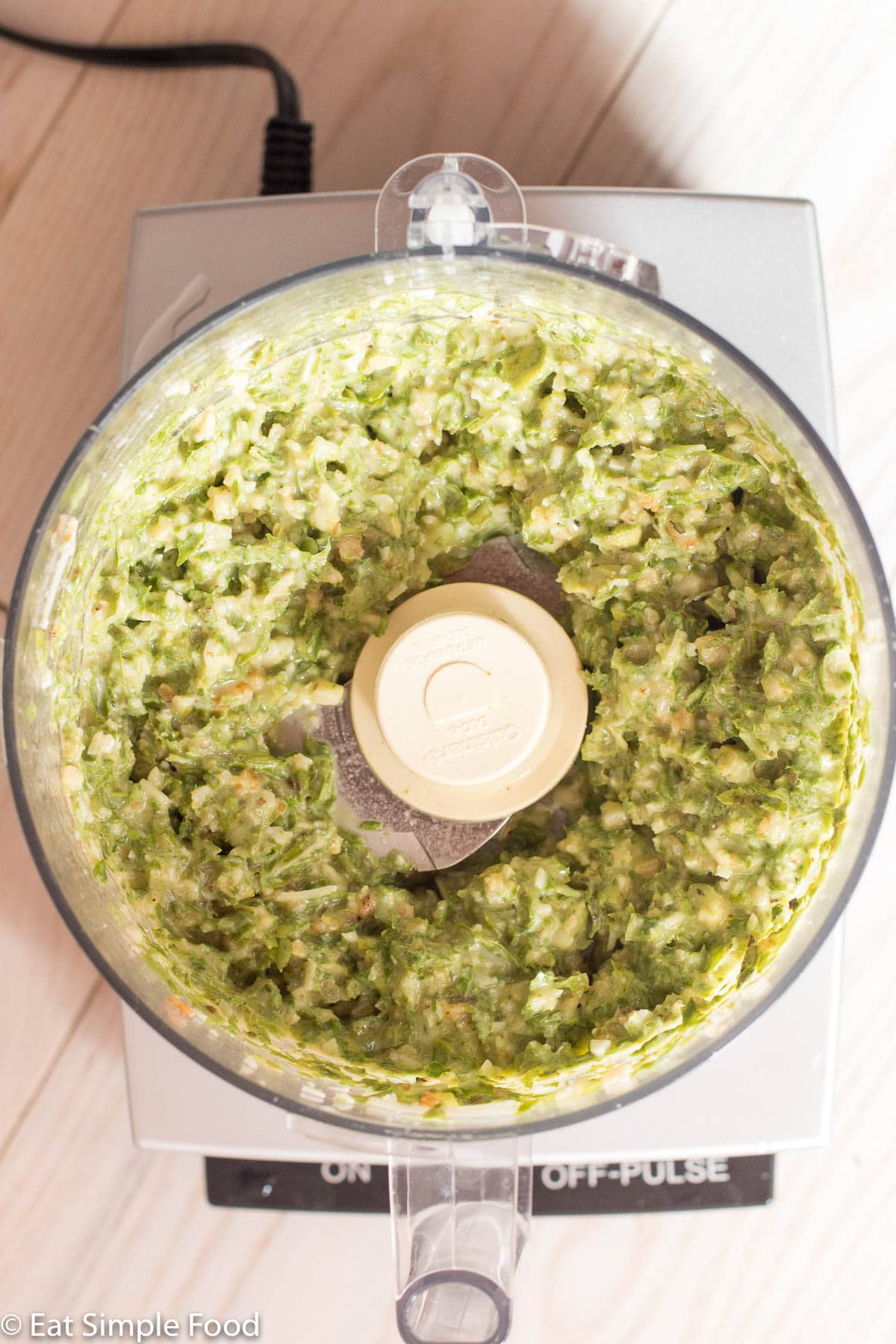 Chunky light green basil pesto in a food processor with the lid off.