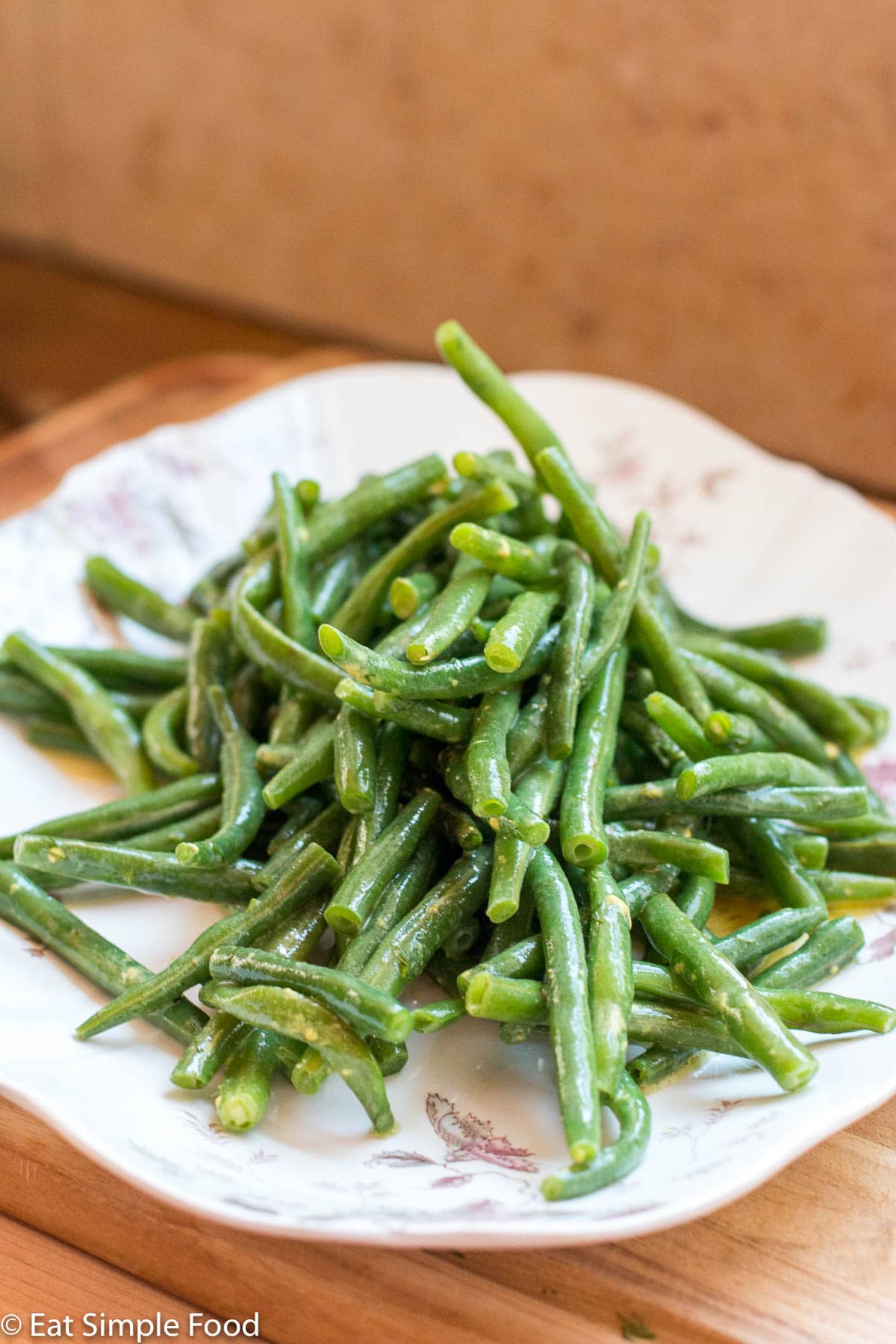 Side view of cooked green beans in a yellow sauce on a white plate on a brown table.