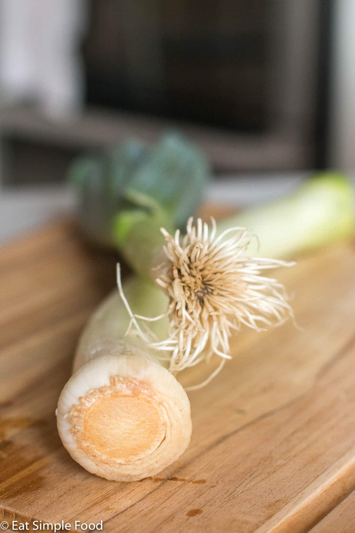 2 whole leeks with the root end facing the camera on a wood cutting board