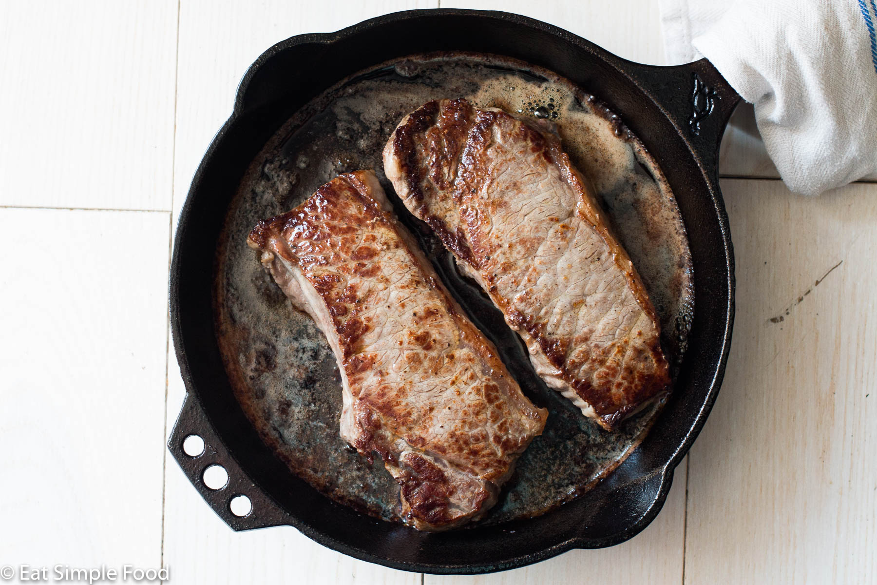 Top down view of two strip steaks in a black cast iron pan with a browned sauce at the bottom of the pan.