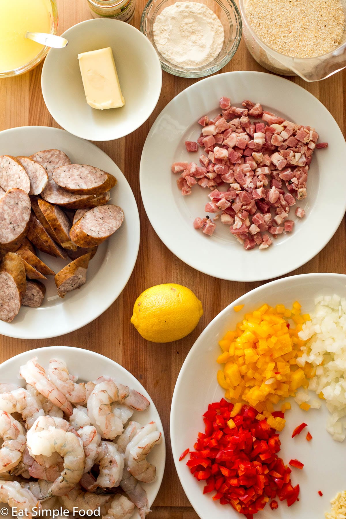 Raw peeled and devined shrimp, red and yellow peppers diced, diced onions, sliced preserved sausage, raw diced pancetta, butter bowl, bowl of flour, bowl of grits, bowl of broth, one whole lemon.