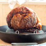 Browned prime rib roast on elevated rack in a cast iron pan on a wood cutting board. Close up.