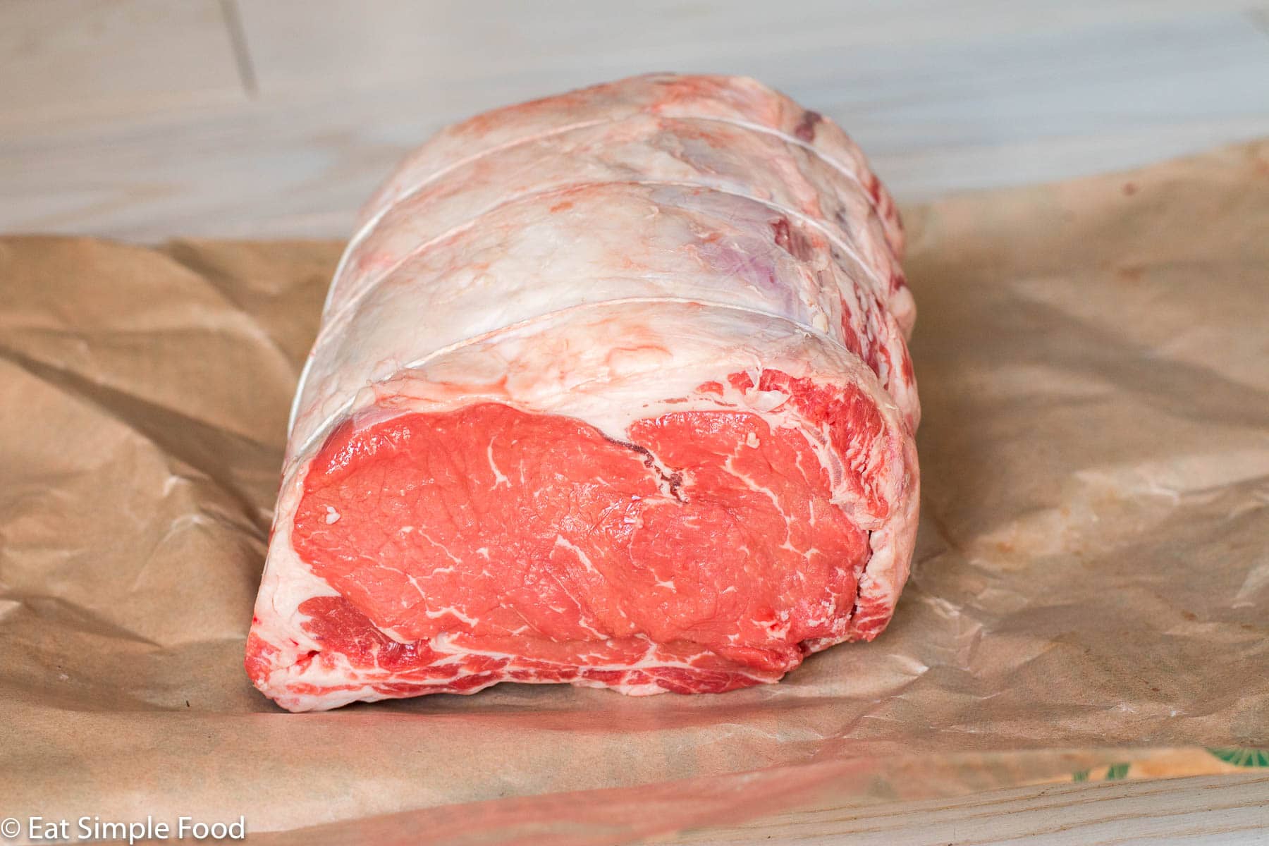 Raw 3 bone in prime rib roast on brown butcher paper. Side view.