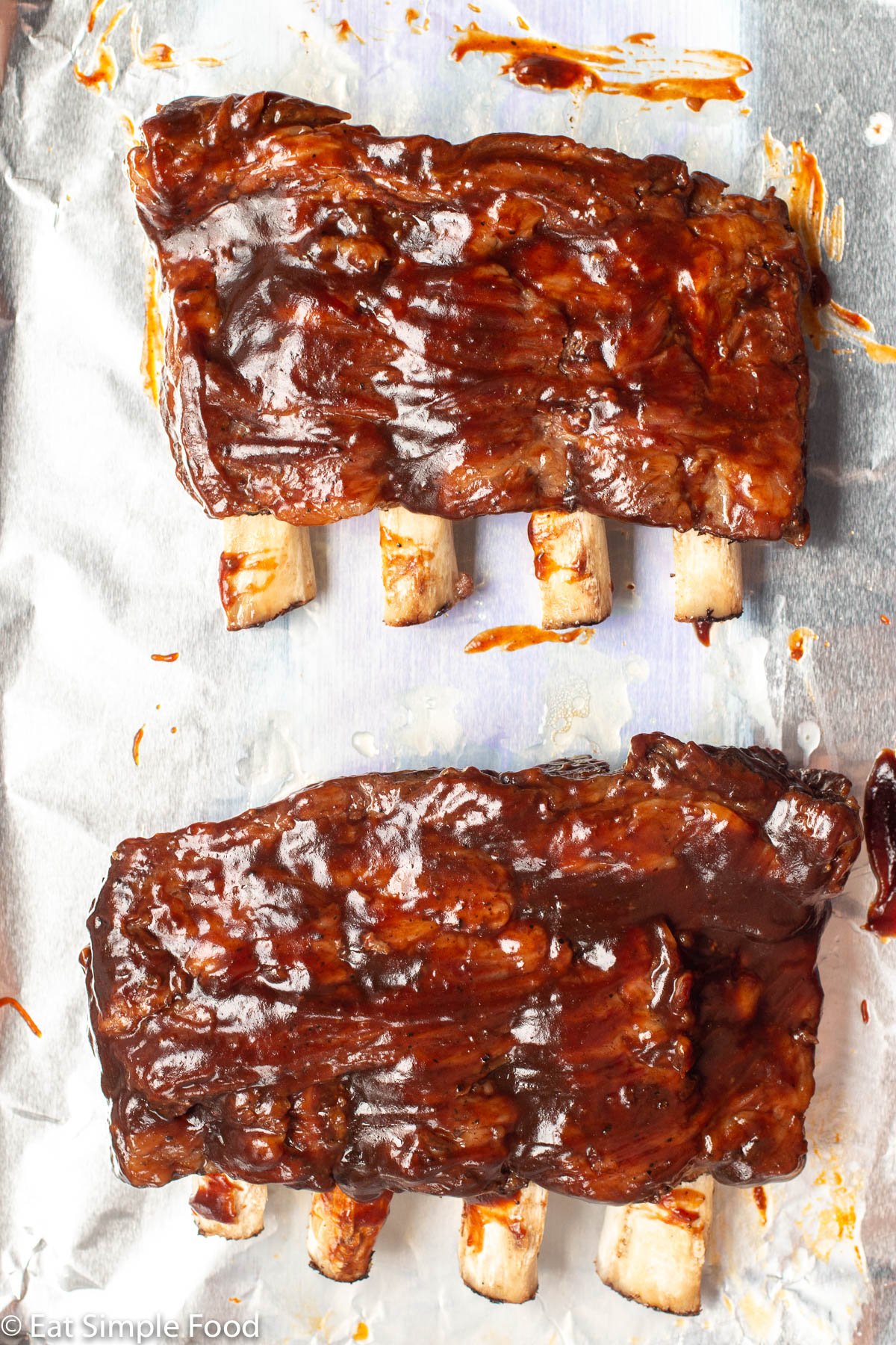 2 racks of beef back ribs slathered in barbecue sauce on an aluminum lined sheet pan.
