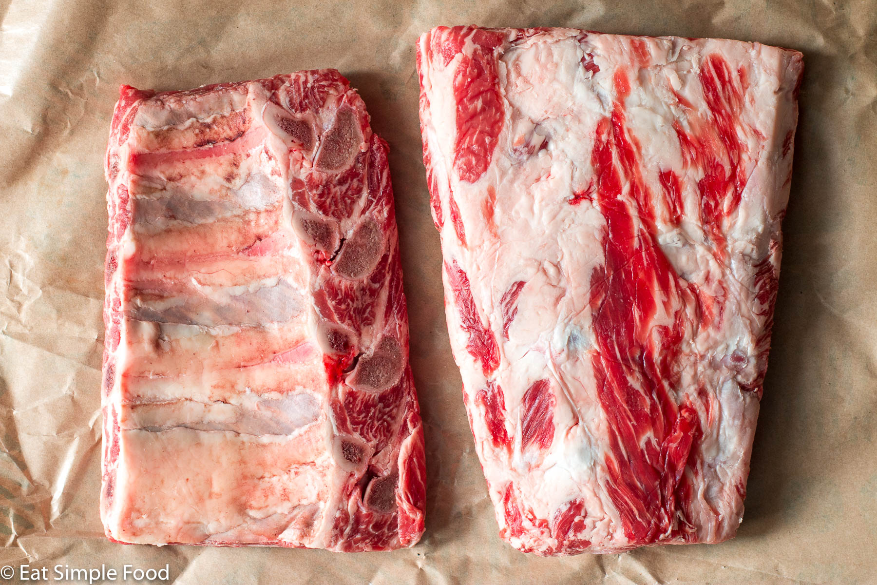 2 racks of beef back ribs. One rack has bone side up. One rack has marbled meat side up.