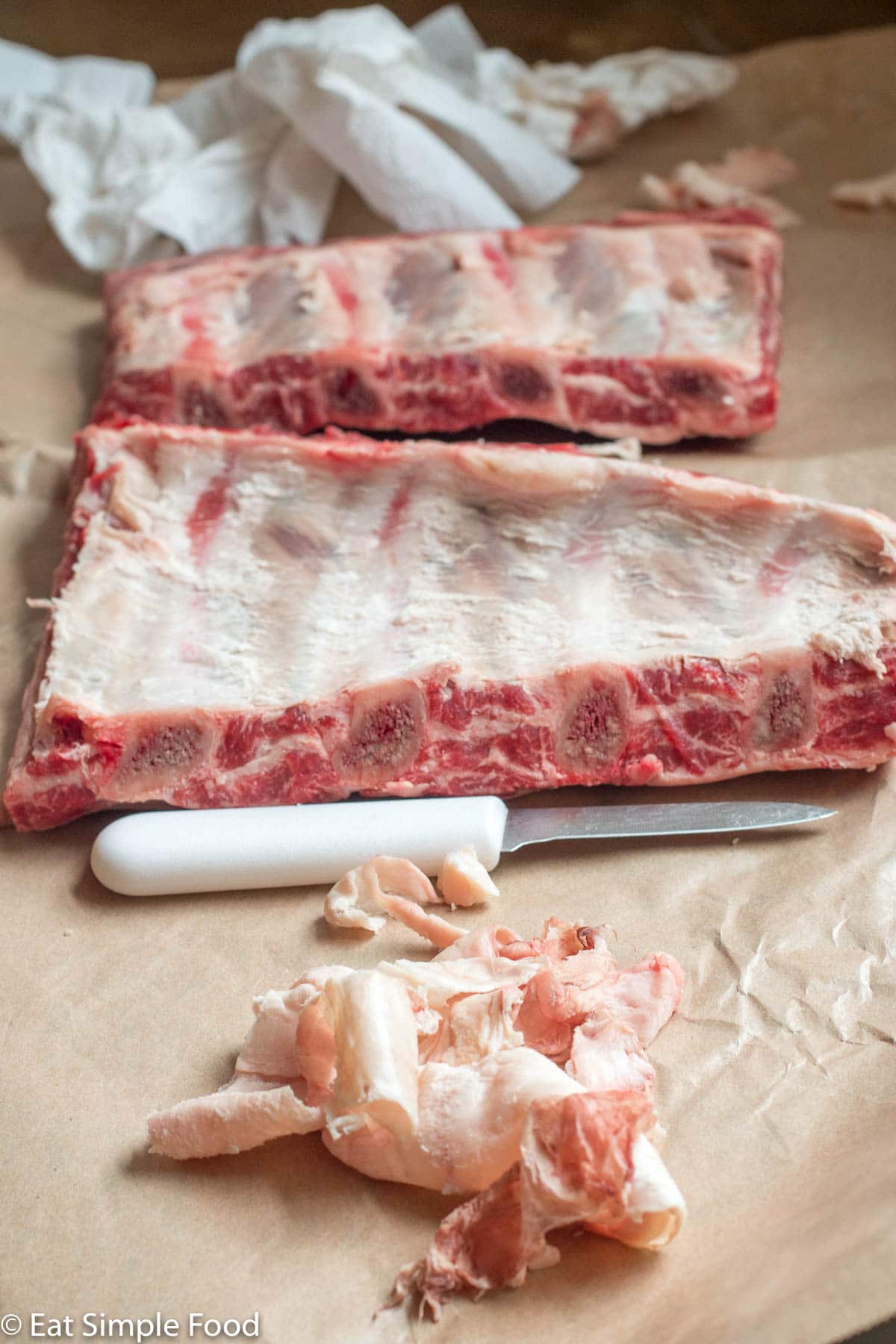 2 racks of beef ribs on butcher's paper with a paring knife and paper towels in the background and white membrane in the front.